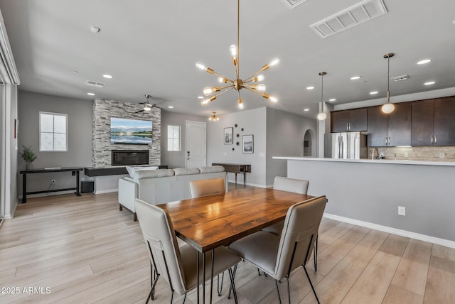 dining space with ceiling fan, a stone fireplace, light wood-style flooring, recessed lighting, and visible vents