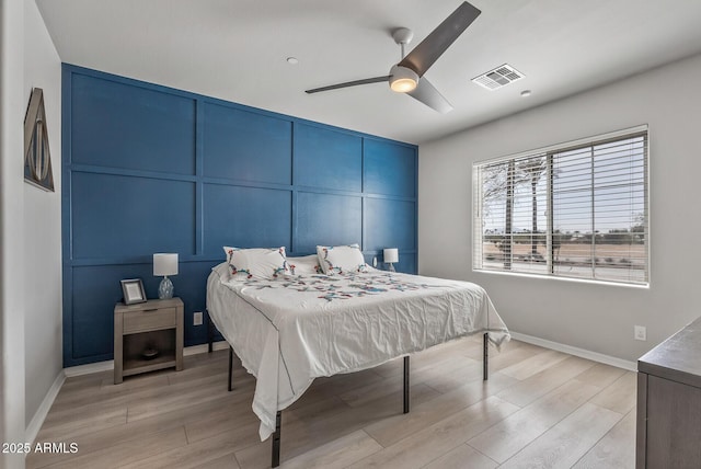 bedroom with light wood-style floors, visible vents, and a decorative wall