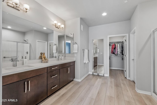 full bath featuring double vanity, a sink, a shower stall, wood finished floors, and baseboards