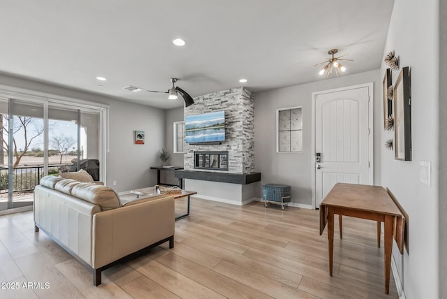 living area featuring light wood-type flooring, visible vents, ceiling fan, and a stone fireplace