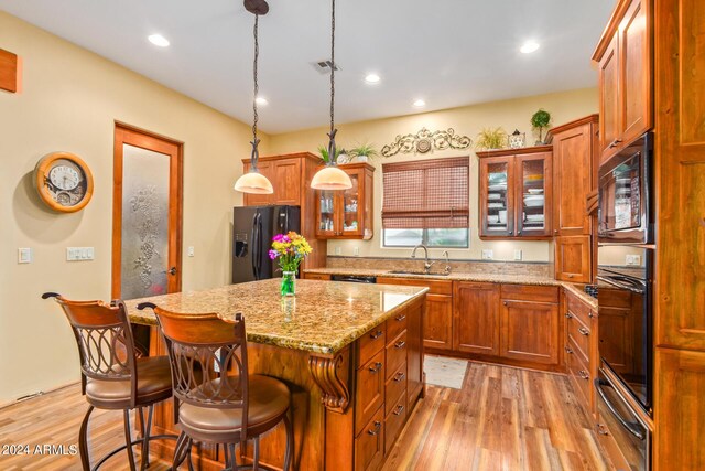 kitchen with light hardwood / wood-style floors, a kitchen island, hanging light fixtures, and black appliances