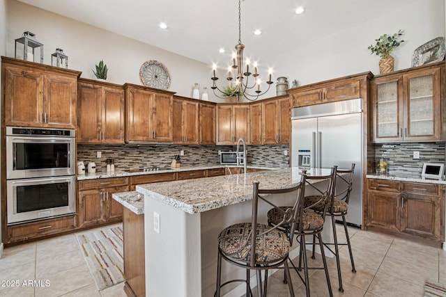 42429 N Cross Timbers Ct, Anthem, AZ 85086 - kitchen featuring stainless steel appliances, light tile patterned floors, tasteful backsplash, brown cabinets, and an island with sink