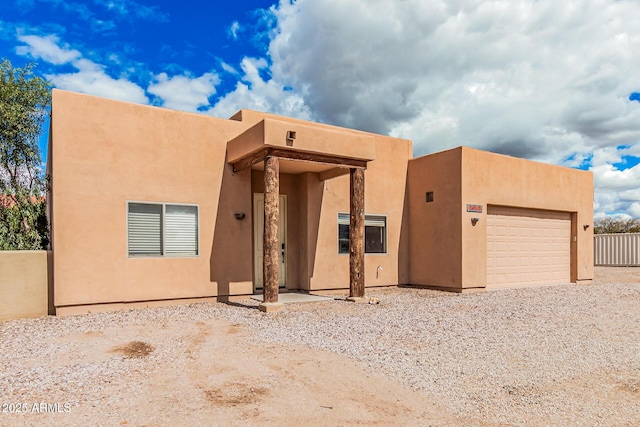 pueblo-style home featuring stucco siding, driveway, a garage, and fence