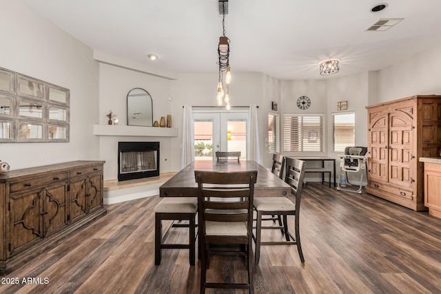 dining area featuring dark wood-style floors, visible vents, a fireplace with raised hearth, and french doors