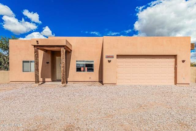 pueblo revival-style home with stucco siding, driveway, and a garage