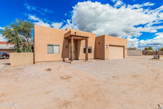 pueblo-style home with stucco siding, a garage, gravel driveway, and fence