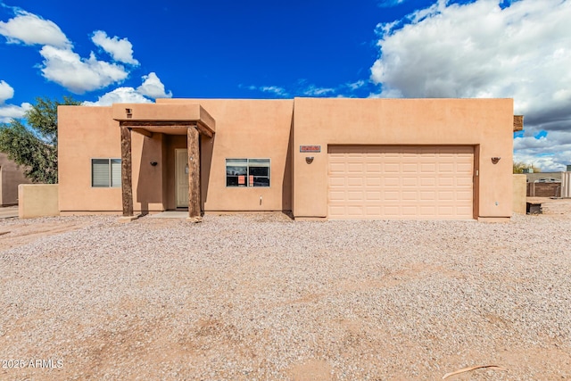 pueblo-style house with stucco siding, gravel driveway, and a garage