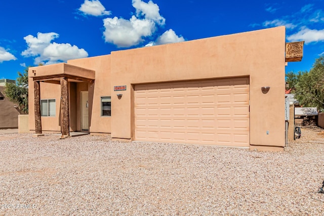 pueblo-style home with stucco siding, a garage, and gravel driveway