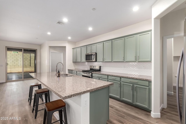 kitchen with sink, stainless steel appliances, a kitchen breakfast bar, light stone counters, and a center island with sink