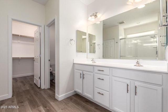 bathroom featuring wood-type flooring, toilet, a shower with door, and vanity