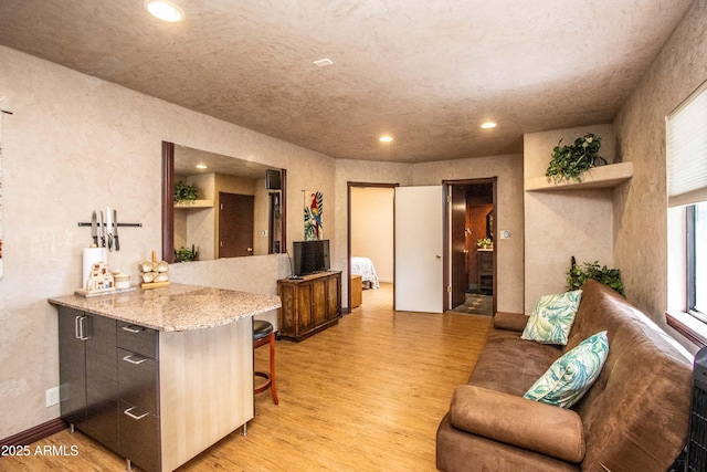 6334 E Albany St, Mesa, AZ 85205 - kitchen featuring light wood-style flooring, a breakfast bar area, recessed lighting, light stone countertops, and a textured wall