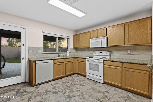 kitchen with white appliances, light stone counters, decorative backsplash, and a sink