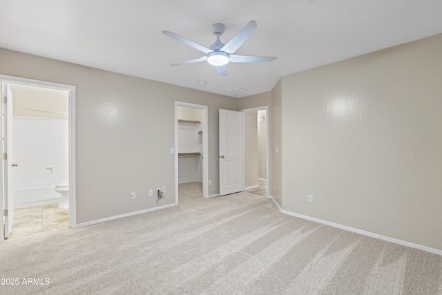 unfurnished bedroom with light colored carpet, ceiling fan, ensuite bathroom, baseboards, and a spacious closet