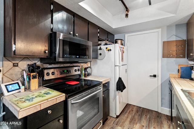 kitchen featuring wood-type flooring, tasteful backsplash, tile counters, dark brown cabinets, and stainless steel appliances