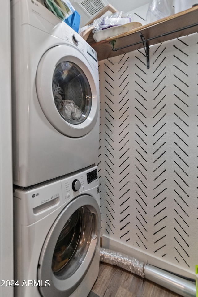 laundry area with hardwood / wood-style floors and stacked washer and clothes dryer