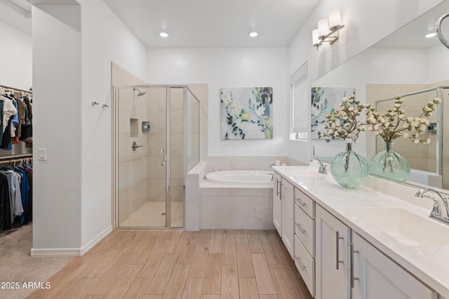 full bathroom with a garden tub, wood finished floors, a spacious closet, a sink, and a stall shower