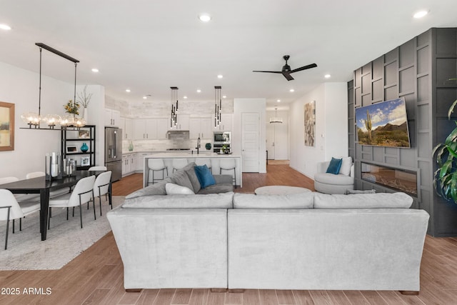living room with light wood-style floors, ceiling fan with notable chandelier, and recessed lighting