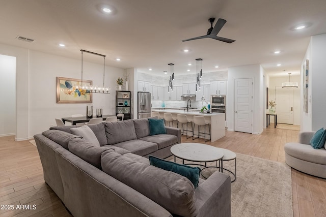 living room with light wood-type flooring, recessed lighting, baseboards, and ceiling fan with notable chandelier