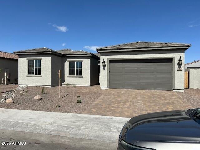 view of front facade with an attached garage, an outdoor structure, decorative driveway, and stucco siding