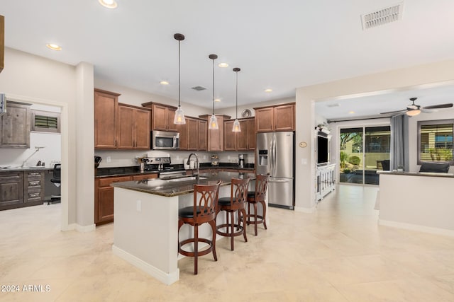 kitchen with sink, a kitchen bar, hanging light fixtures, stainless steel appliances, and a center island with sink