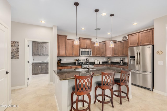 kitchen featuring hanging light fixtures, dark stone counters, a center island with sink, sink, and appliances with stainless steel finishes