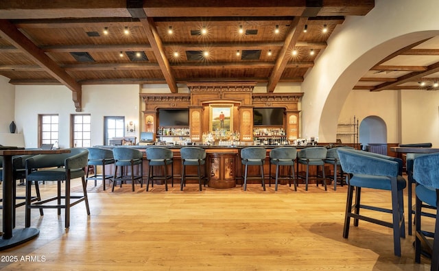 bar featuring beam ceiling, wooden ceiling, a towering ceiling, and light wood-type flooring