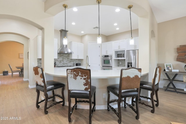 kitchen with appliances with stainless steel finishes, decorative light fixtures, white cabinetry, and wall chimney range hood