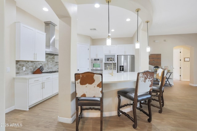 kitchen featuring backsplash, white cabinets, wall chimney exhaust hood, decorative light fixtures, and stainless steel appliances