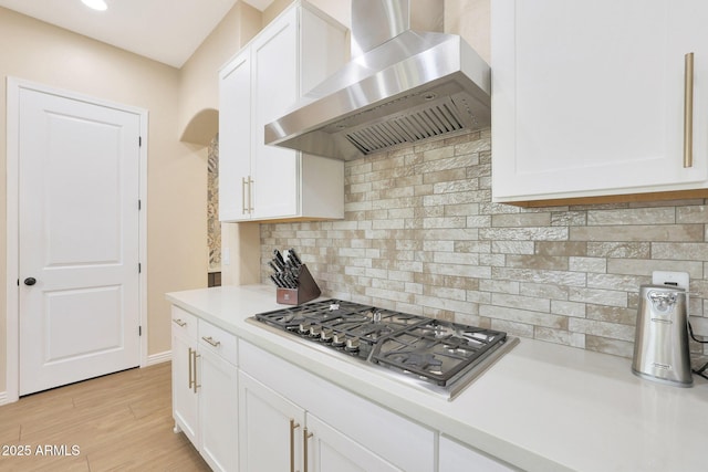 kitchen with stainless steel gas stovetop, wall chimney exhaust hood, white cabinetry, and decorative backsplash