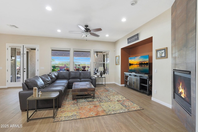 living room featuring a tile fireplace, ceiling fan, and light hardwood / wood-style floors