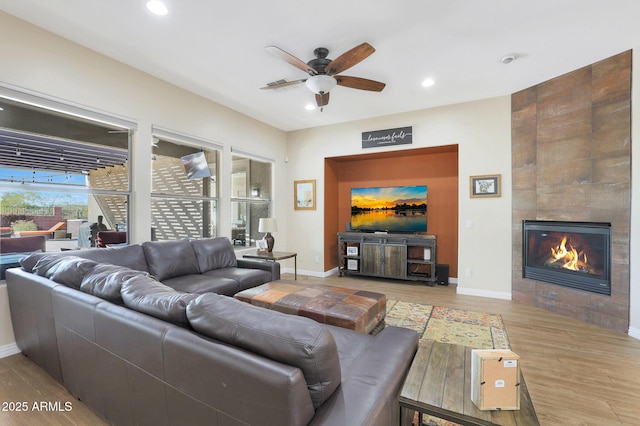 living room with a tile fireplace, ceiling fan, and light hardwood / wood-style floors