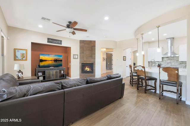 living room with ceiling fan, light hardwood / wood-style floors, sink, and a tile fireplace