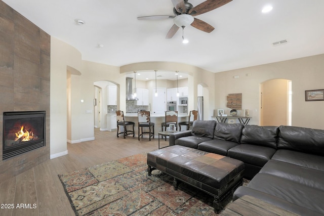 living room featuring a tiled fireplace, ceiling fan, and light hardwood / wood-style flooring