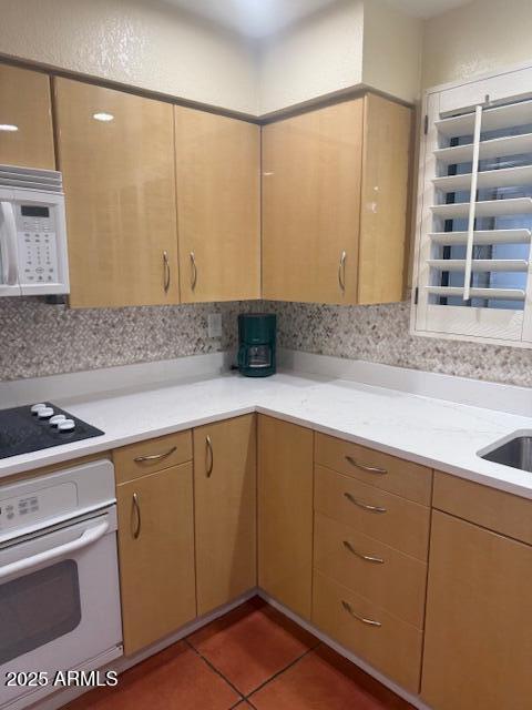 kitchen featuring light brown cabinets, dark tile patterned flooring, white appliances, and decorative backsplash