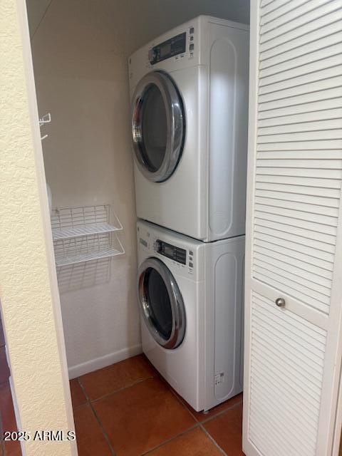 laundry room featuring stacked washer / drying machine and dark tile patterned flooring