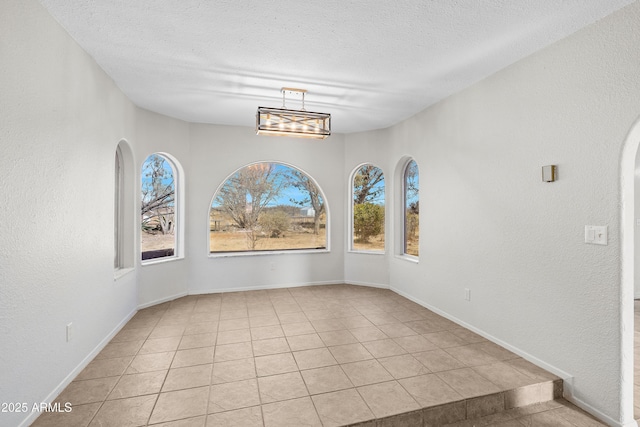 unfurnished dining area featuring baseboards, light tile patterned flooring, a textured ceiling, and a textured wall