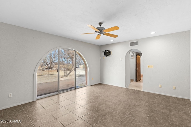 spare room with arched walkways, visible vents, a textured wall, ceiling fan, and baseboards