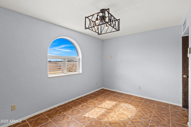 spare room with a chandelier, visible vents, a textured wall, and baseboards