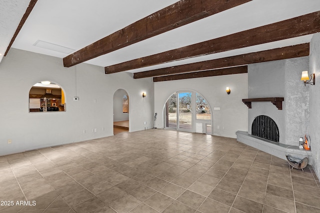 unfurnished living room with arched walkways, a fireplace with raised hearth, beam ceiling, and tile patterned floors