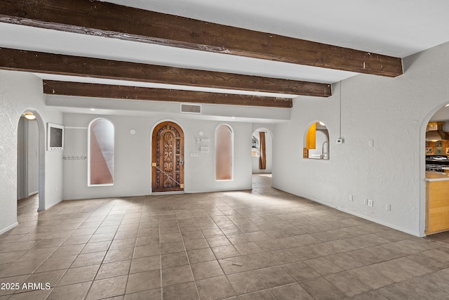 interior space featuring arched walkways, a textured wall, beamed ceiling, and visible vents