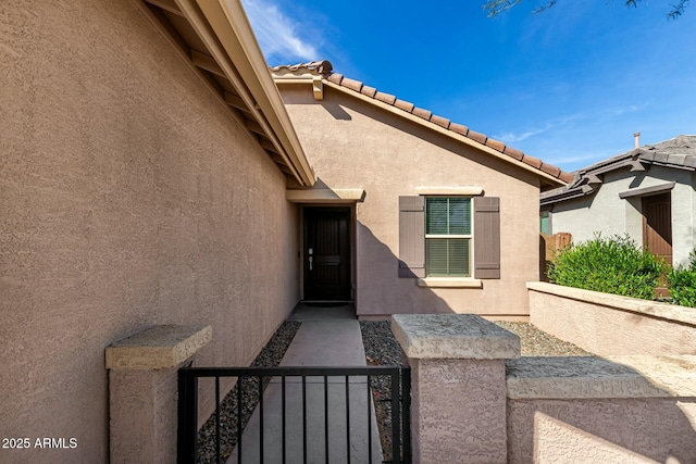 entrance to property with a tile roof, fence, and stucco siding