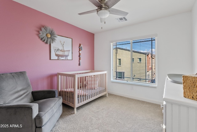 bedroom featuring a crib, light colored carpet, and ceiling fan