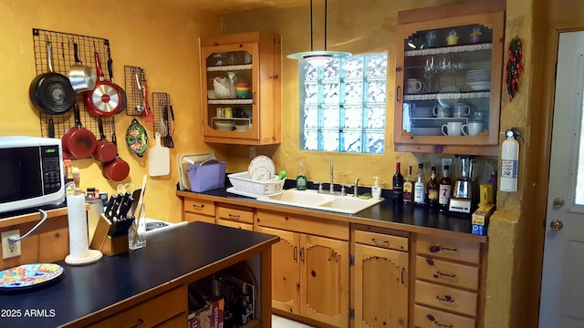 kitchen featuring dark countertops, white microwave, glass insert cabinets, and a sink