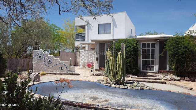 view of front facade with fence, a balcony, and stucco siding