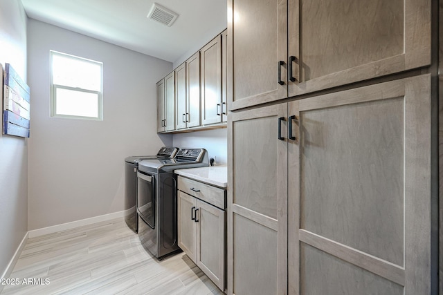 clothes washing area with visible vents, cabinet space, light wood finished floors, baseboards, and washing machine and clothes dryer