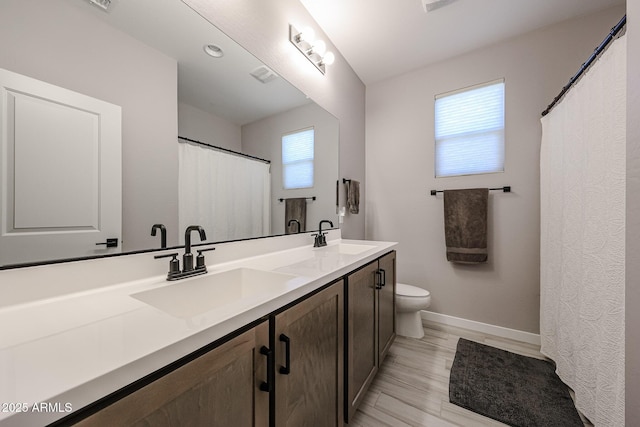 full bath featuring a sink, baseboards, toilet, and double vanity