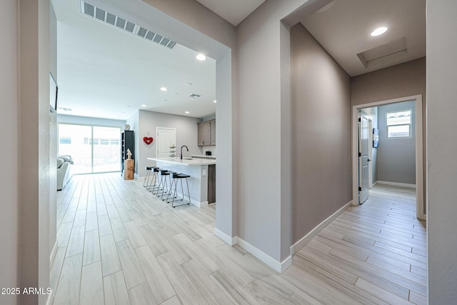 hallway with visible vents, a sink, baseboards, and wood tiled floor