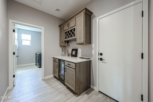 bar featuring beverage cooler, visible vents, baseboards, and light wood-style floors