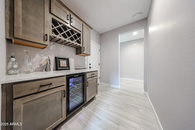 kitchen with light wood-style flooring, baseboards, beverage cooler, and light stone countertops