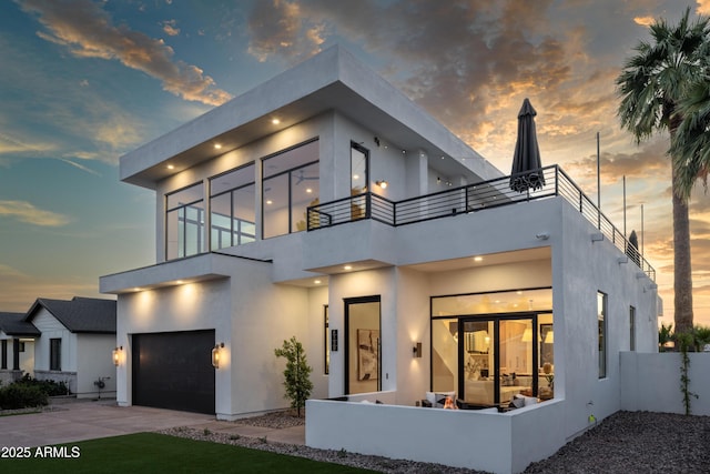 modern home featuring a balcony, an attached garage, concrete driveway, and stucco siding